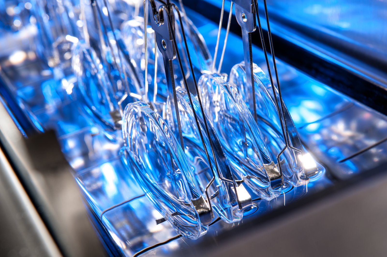 Ophthalmic lenses held in clips on a dip carrier being coated inside a Unitech Shyre HC200 dip hardcoating system